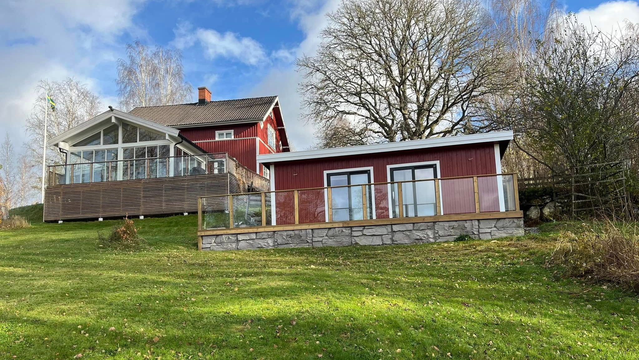 Rødt hus og anneks i landlig hage med grønt gress.