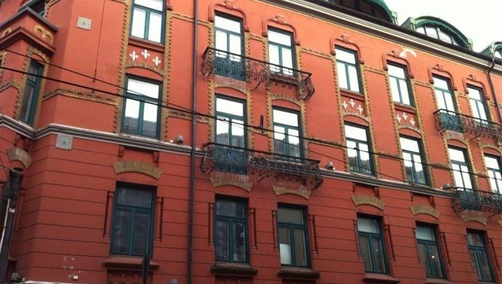 Rødt bygg med balkonger og apotek i første etasje.